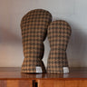 Two golf club headcovers in a brown and tan houndstooth pattern, standing on a wooden surface against a light gray brick wall